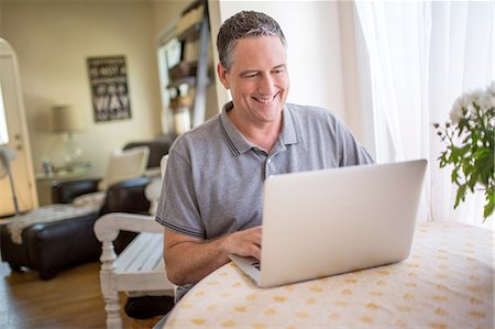 Mature man typing on laptop at kitchen table Stock Photo - Premium Royalty-Free, Code: 614-08270220