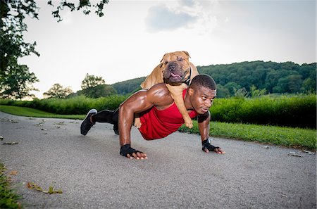 Young man doing pushups on rural road whilst giving dog a piggyback Foto de stock - Sin royalties Premium, Código: 614-08270509