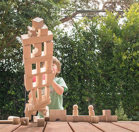 Young boy pushing over wooden structure made from building blocks, outdoors Foto de stock - Sin royalties Premium, Código: 614-08307572