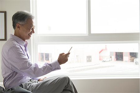 Side view of mature man sitting in front of window using smartphone Fotografie stock - Premium Royalty-Free, Codice: 614-08307892