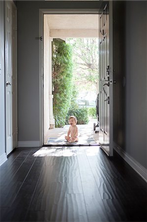 View through entrance hall of baby boy sitting outside at open front door, looking at camera open mouthed Stock Photo - Premium Royalty-Free, Code: 614-08308002