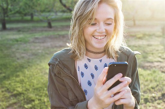 Head and shoulders of young woman using smartphone looking down smiling Stock Photo - Premium Royalty-Free, Image code: 614-08308087