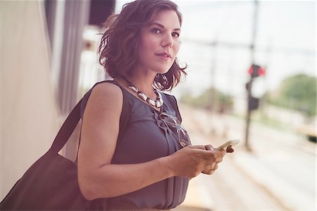 Mid adult woman waiting at train station, holding smartphone Stock Photo - Premium Royalty-Free, Code: 614-08329188