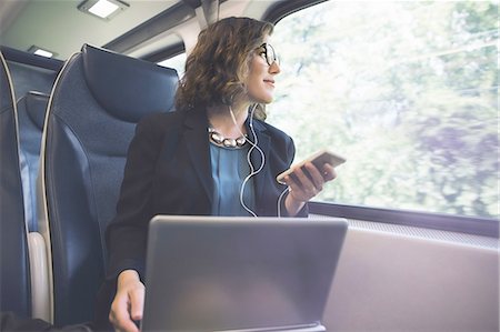 Mid adult woman on train, holding smartphone, laptop in front of her Stock Photo - Premium Royalty-Free, Code: 614-08329209