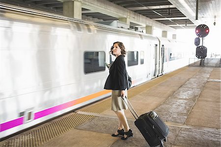 Mid adult woman waiting to board train, holding wheeled suitcase and smartphone Stockbilder - Premium RF Lizenzfrei, Bildnummer: 614-08329203