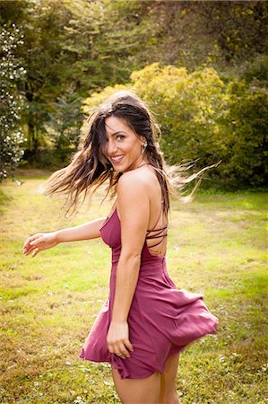 simsearch:614-08329271,k - Mid adult woman wearing short dress dancing on grass, looking over shoulder at camera smiling Photographie de stock - Premium Libres de Droits, Code: 614-08329273