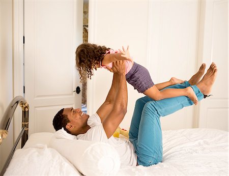 family at home playing - Side view of father lying on bed to lifting up daughter, face to face smiling Stock Photo - Premium Royalty-Free, Code: 614-08329303