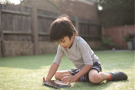 Boy in garden sitting on grass looking down using digital tablet Stock Photo - Premium Royalty-Free, Code: 614-08329328