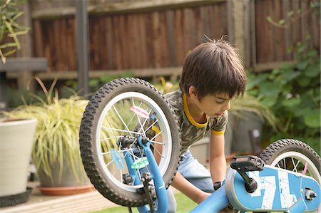 Boy in garden repairing upside down bicycle looking down Stock Photo - Premium Royalty-Free, Code: 614-08329320