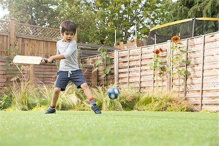 Boy playing cricket in garden, ball in mid air Stock Photo - Premium Royalty-Free, Code: 614-08329322