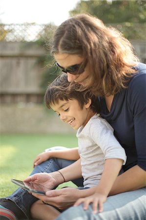 Side view of boy sitting on mother's lap using digital tablet looking down smiling Stock Photo - Premium Royalty-Free, Code: 614-08329330