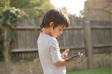 Side view of boy in garden looking down using digital tablet Stock Photo - Premium Royalty-Free, Code: 614-08329332