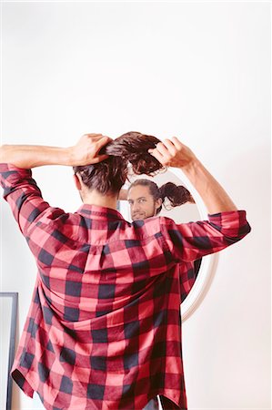 Young man looking in mirror, putting hair in ponytail, rear view Foto de stock - Sin royalties Premium, Código: 614-08329398