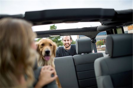 Young woman in jeep looking over her shoulder at dog and boyfriend Foto de stock - Sin royalties Premium, Código: 614-08329405