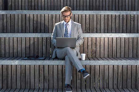 Suited young businessman typing on laptop on city stair Stock Photo - Premium Royalty-Free, Code: 614-08329502