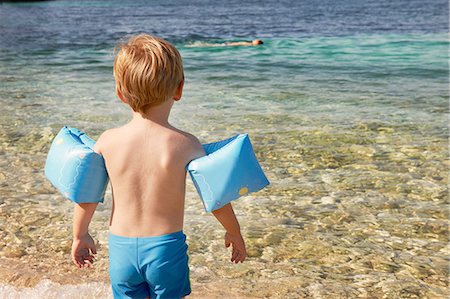 rear view boy swimsuit - Rear view of cute boy wearing blue armbands paddling in sea Stock Photo - Premium Royalty-Free, Code: 614-08383460