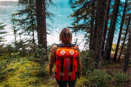 High angle rear view of mid adult woman carrying orange colour backpack standing in forest looking at water, Moraine lake, Banff National Park, Alberta Canada Stock Photo - Premium Royalty-Free, Code: 614-08383508