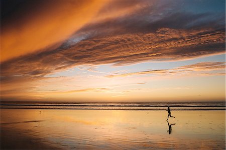 Side view of mid adult nude womans silhouette running on beach under dramatic sky at sunset Photographie de stock - Premium Libres de Droits, Code: 614-08383500