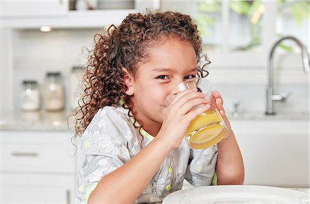 Girl at kitchen counter drinking orange juice looking at camera Foto de stock - Sin royalties Premium, Código: 614-08383715