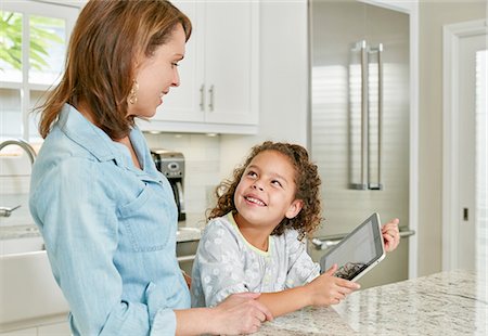 Mother and daughter at kitchen counter using digital tablet, looking up smiling Foto de stock - Sin royalties Premium, Código: 614-08383717