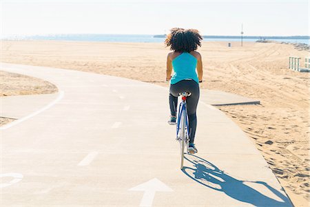 simsearch:614-08392500,k - Mid adult woman cycling on pathway at beach, rear view Fotografie stock - Premium Royalty-Free, Codice: 614-08392488
