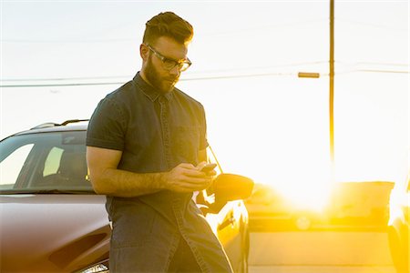 Young man leaning against car, using smartphone Stock Photo - Premium Royalty-Free, Code: 614-08392529