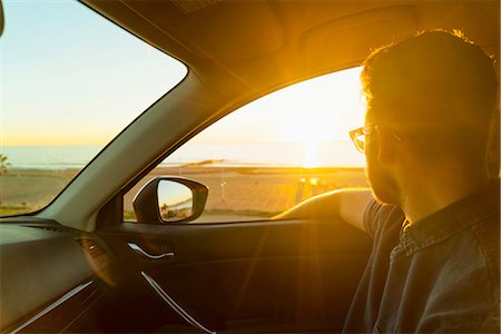 Young man looking out of car window at sunset Stock Photo - Premium Royalty-Free, Code: 614-08392533