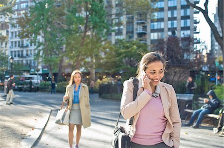 Young woman talking on smartphone whilst walking through city park Stock Photo - Premium Royalty-Free, Code: 614-08392569
