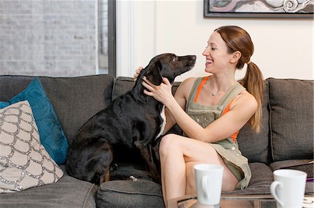 dogs on couch - Young woman sitting on sofa face to face with pet dog smiling Stock Photo - Premium Royalty-Free, Code: 614-08392604