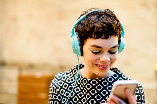Mid adult woman, wearing headphones, looking at smartphone, smiling Stock Photo - Premium Royalty-Free, Image code: 614-08392634