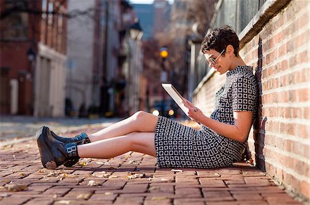 skype - Mid adult woman sitting against brick wall, using digital tablet Photographie de stock - Premium Libres de Droits, Code: 614-08392630