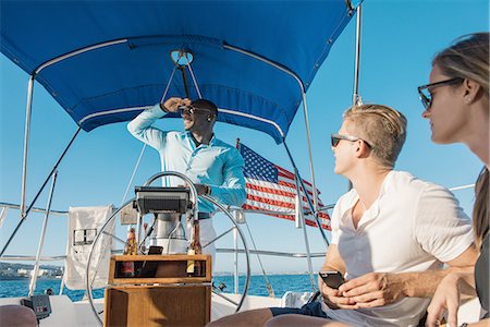simsearch:614-08392689,k - Man behind wheel of sailboat, enjoying view with friends Stock Photo - Premium Royalty-Free, Code: 614-08392684