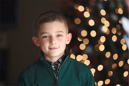 Portrait of boy in front of christmas tree looking at camera smiling Stock Photo - Premium Royalty-Free, Code: 614-08392719