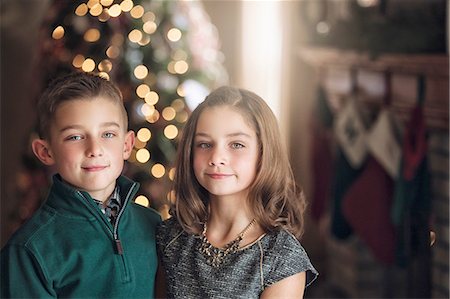 Portrait of girl and boy in front of christmas tree looking at camera smiling Stock Photo - Premium Royalty-Free, Code: 614-08392725