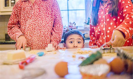 simsearch:614-08946613,k - Boy in kitchen making cookies with sisters peeking over kitchen counter looking at camera Photographie de stock - Premium Libres de Droits, Code: 614-08392734