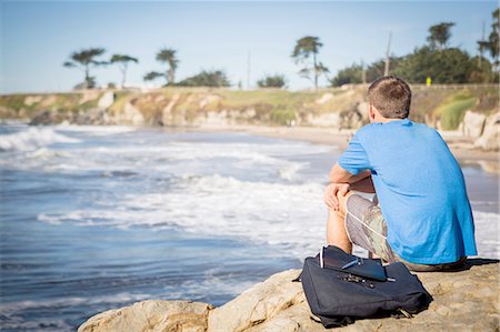 simsearch:614-08081220,k - Young man sitting by rock, looking out to sea, rear view Fotografie stock - Premium Royalty-Free, Codice: 614-08487834