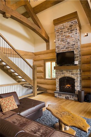 fonte - Living room with leather sofa and coffee table in front of  stone fireplace and stairs with iron railings in Scandinavian cottage style log home Photographie de stock - Premium Libres de Droits, Code: 614-08488008