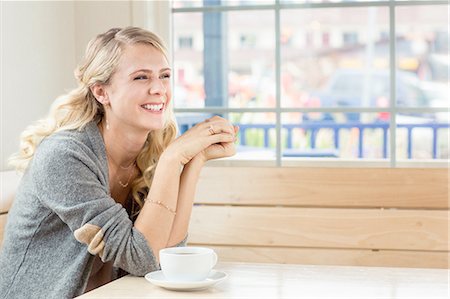 simsearch:614-07031976,k - Young woman sitting at table with tea and saucer, resting on elbows, looking away smiling Stock Photo - Premium Royalty-Free, Code: 614-08488011