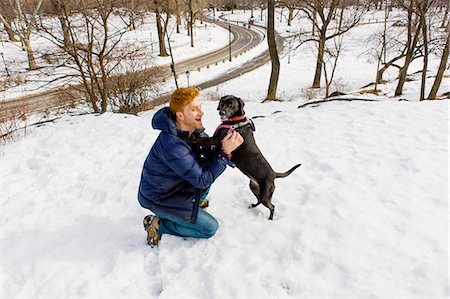 Young man petting dog in snowy Central Park, New York, USA Stock Photo - Premium Royalty-Free, Code: 614-08535570