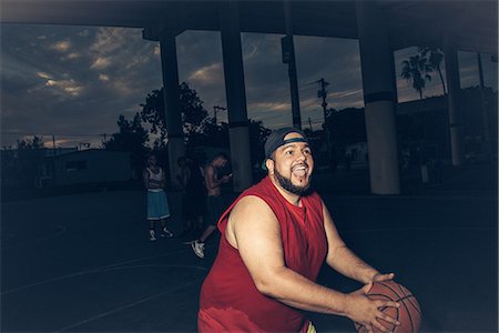 fat men in undershirts - Mid adult man wearing vest playing basketball open mouthed smiling Stock Photo - Premium Royalty-Free, Code: 614-08535656