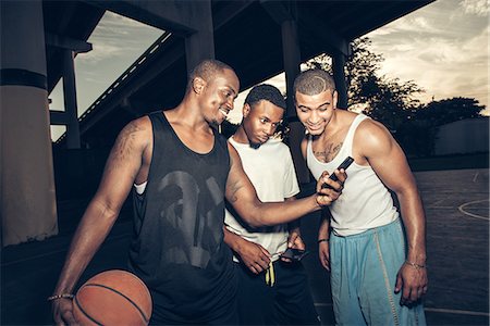 simsearch:614-08535671,k - Young men holding basketball looking at smartphone smiling Photographie de stock - Premium Libres de Droits, Code: 614-08535660