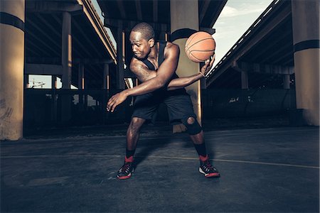simsearch:614-08535671,k - Young man bending forward balancing basketball on hand, looking away Photographie de stock - Premium Libres de Droits, Code: 614-08535661