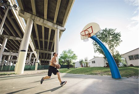 pilar - Side view of young man holding basketball running to basketball hoop Foto de stock - Sin royalties Premium, Código: 614-08535663