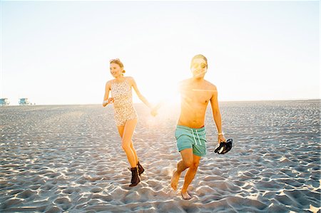 simsearch:614-08544737,k - Young couple wearing swimming costume and shorts running on sunlit beach, Venice Beach, California, USA Photographie de stock - Premium Libres de Droits, Code: 614-08544746