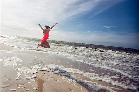 Side view of girl on beach arms raised jumping in mid air Stock Photo - Premium Royalty-Free, Code: 614-08578504