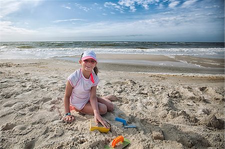 Girl sitting on beach playing in sand, looking at camera smiling Foto de stock - Sin royalties Premium, Código: 614-08578503
