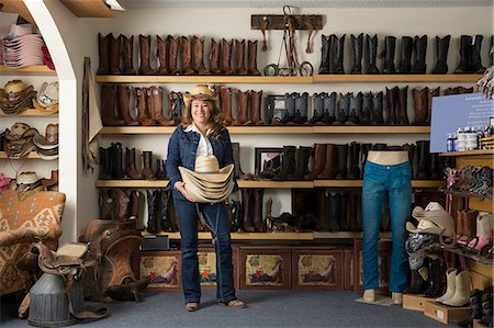 Shop assistant carrying stetsons in front of shelves of boots Photographie de stock - Premium Libres de Droits, Code: 614-08578542