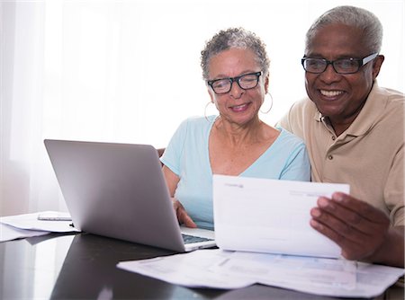 financial happiness - Senior couple sitting at table, using laptop, looking at paperwork Stock Photo - Premium Royalty-Free, Code: 614-08578614