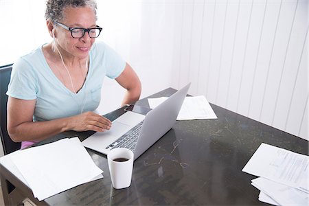 Senior woman sitting at table, using laptop, paperwork on table Stock Photo - Premium Royalty-Free, Code: 614-08578610