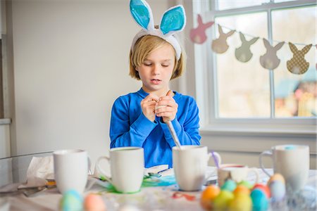 Boy at table wearing bunny ears decorating eggs for Easter Stock Photo - Premium Royalty-Free, Code: 614-08641381